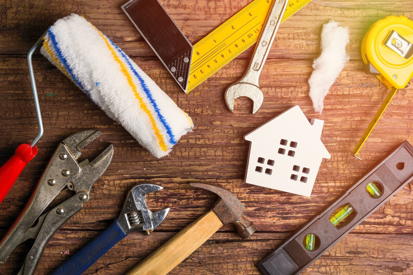 Paint roller, spirit level, spanners, hammer and tape measure laid out around a small model house
