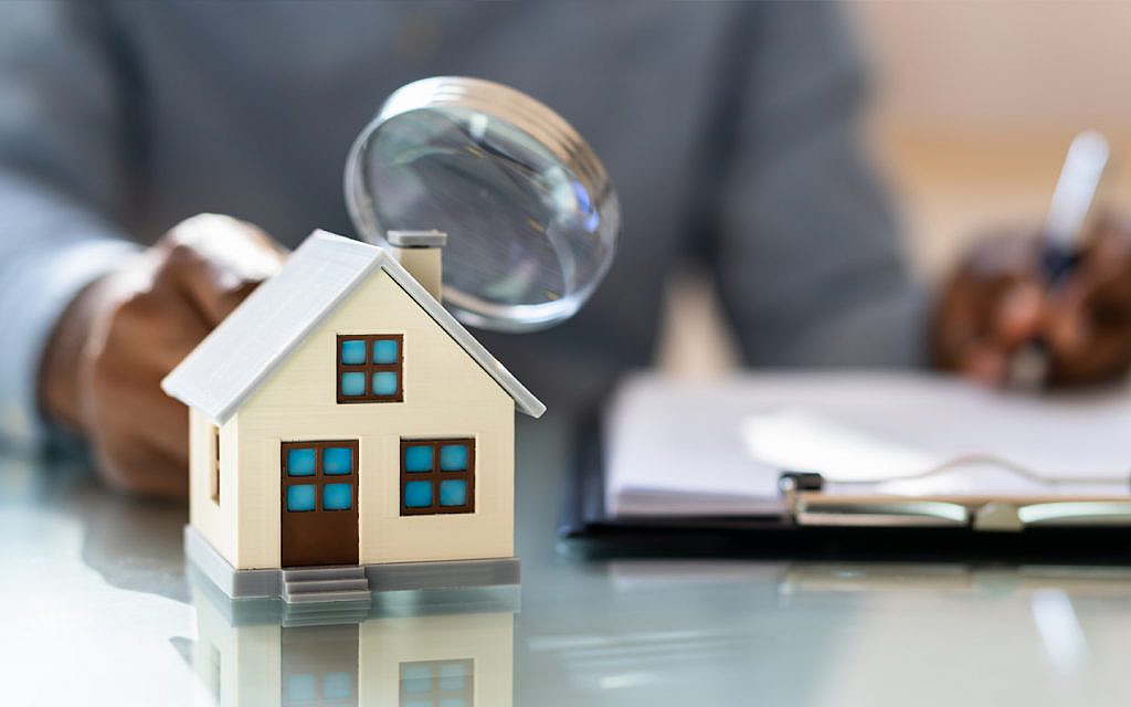 Small model house on a glass desk with a magnifying glass held over it
