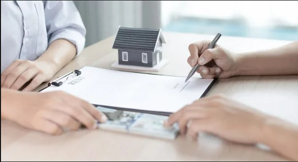 Two people at a table, one signing a rental form, with a small model house beside them